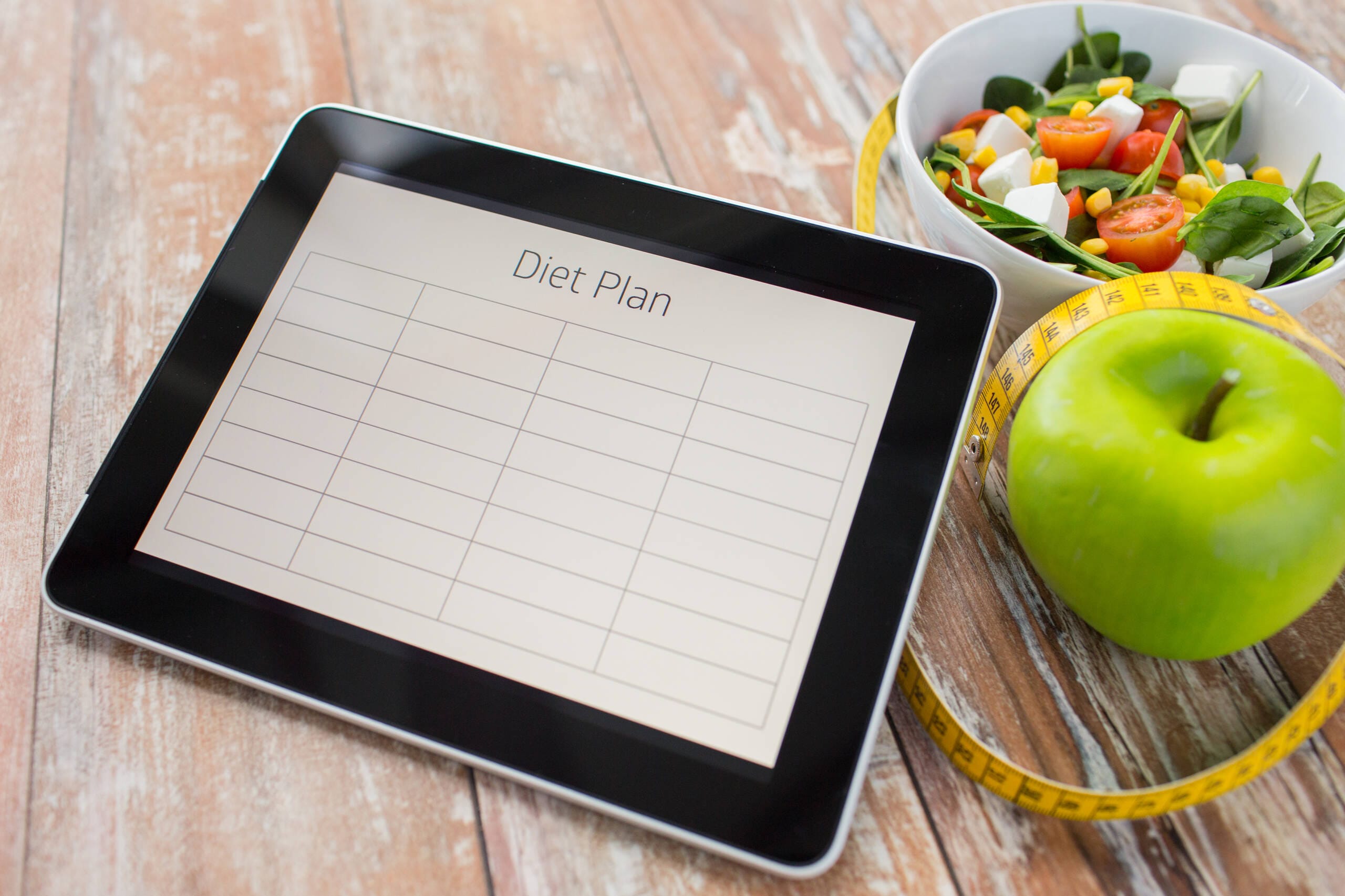 healthy eating dieting weigh loss concept close up diet plan tablet pc screen green apple measuring tape sald scaled
